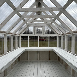 White wooden greenhouse interior with clear roof panels and long benches.
