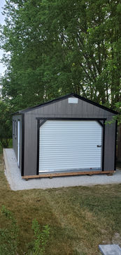 Gray storage shed with white roll-up garage door on concrete slab.