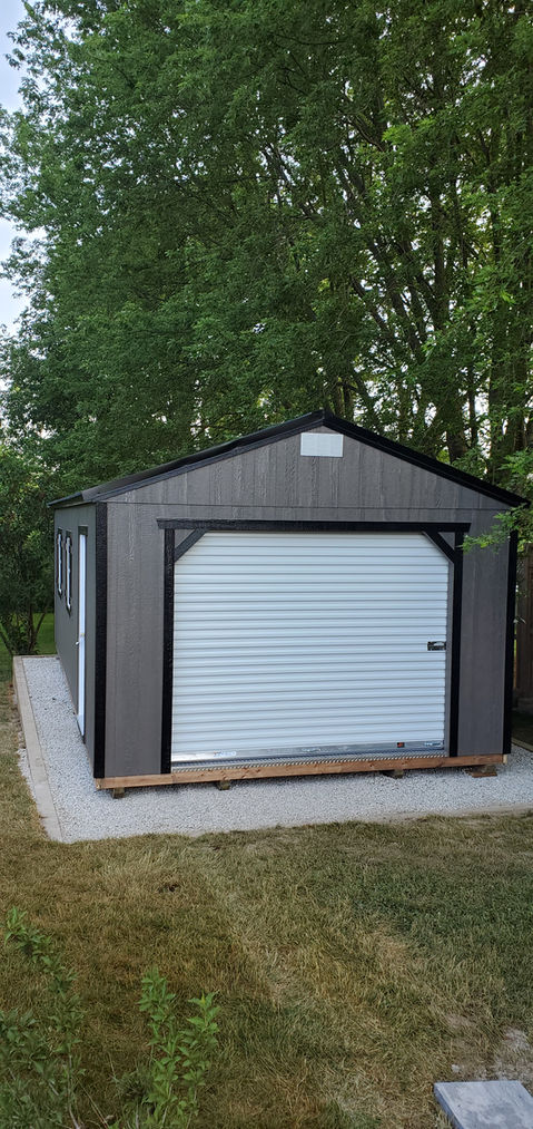 Gray storage shed with white roll-up garage door on concrete slab.
