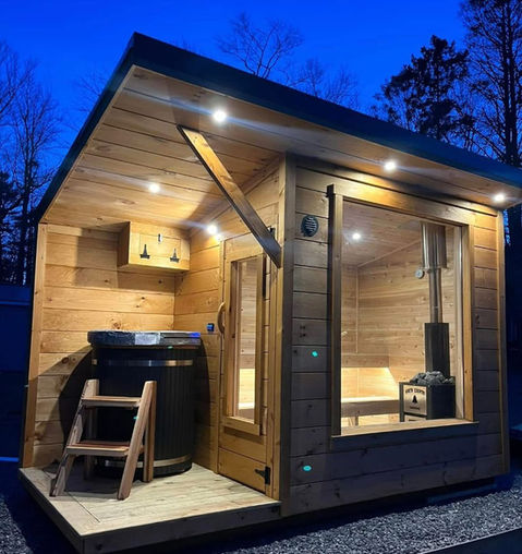 Modern wooden sauna cabin and hot tub lit up at night.