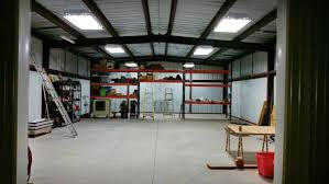 Large empty metal building interior with skylights, shelving, and concrete floor.