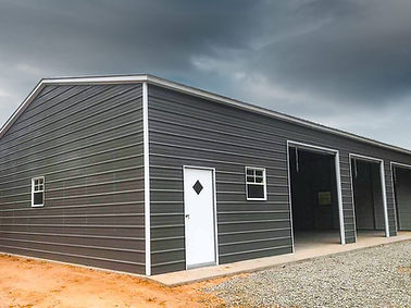 Gray metal building with three open garage bays and a white door.