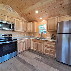 Small rustic kitchen with wood paneled walls, stainless steel appliances.