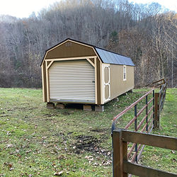 Long tan shed with brown roof, roll-up door, in grassy field.