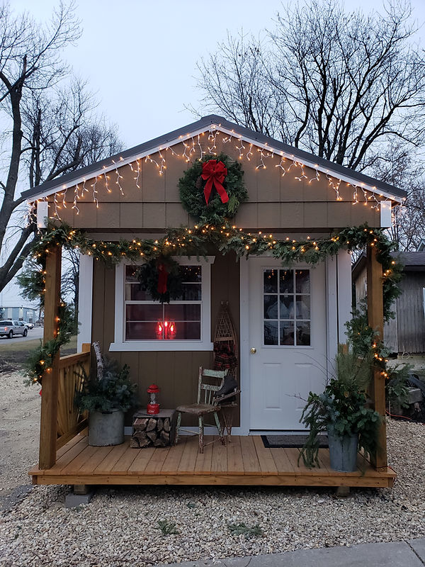 Small brown shed decorated with Christmas lights, wreath, and garland.