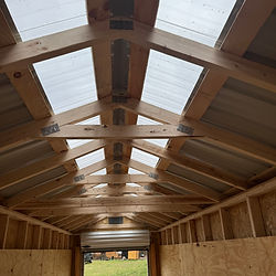 Wooden interior framework of a greenhouse with clear roof panels and light.