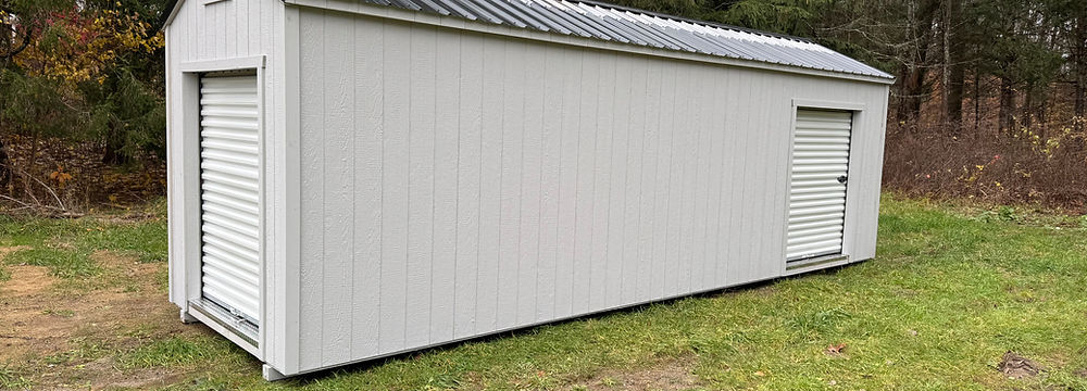 Long white storage shed with roll-up door and hinged door.