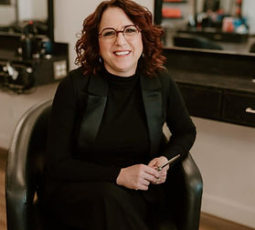 A photo of Michelle Batstone, sitting in a salon chair and smiling at the camera.