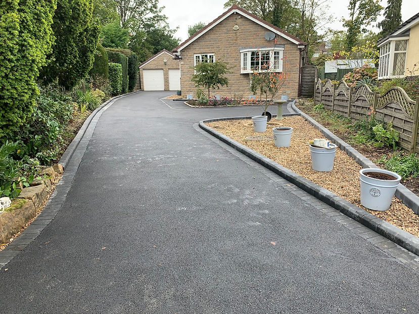 Freshly paved driveway curves towards a double garage, lined with a flowerbed and pots