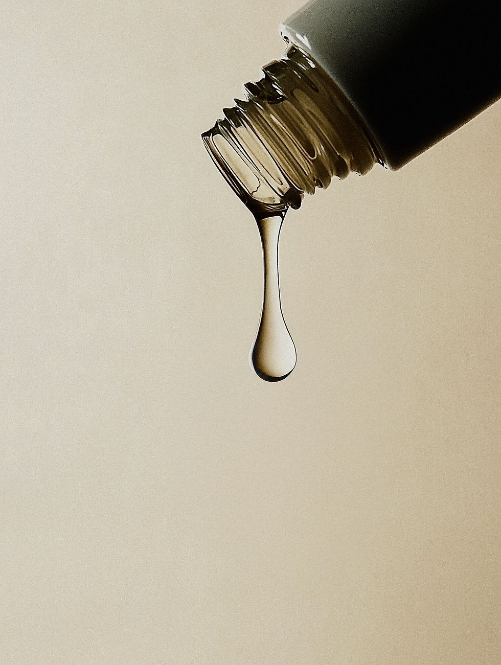 A dropper releasing a single droplet of liquid against a neutral beige background. The scene appears calm and focused.