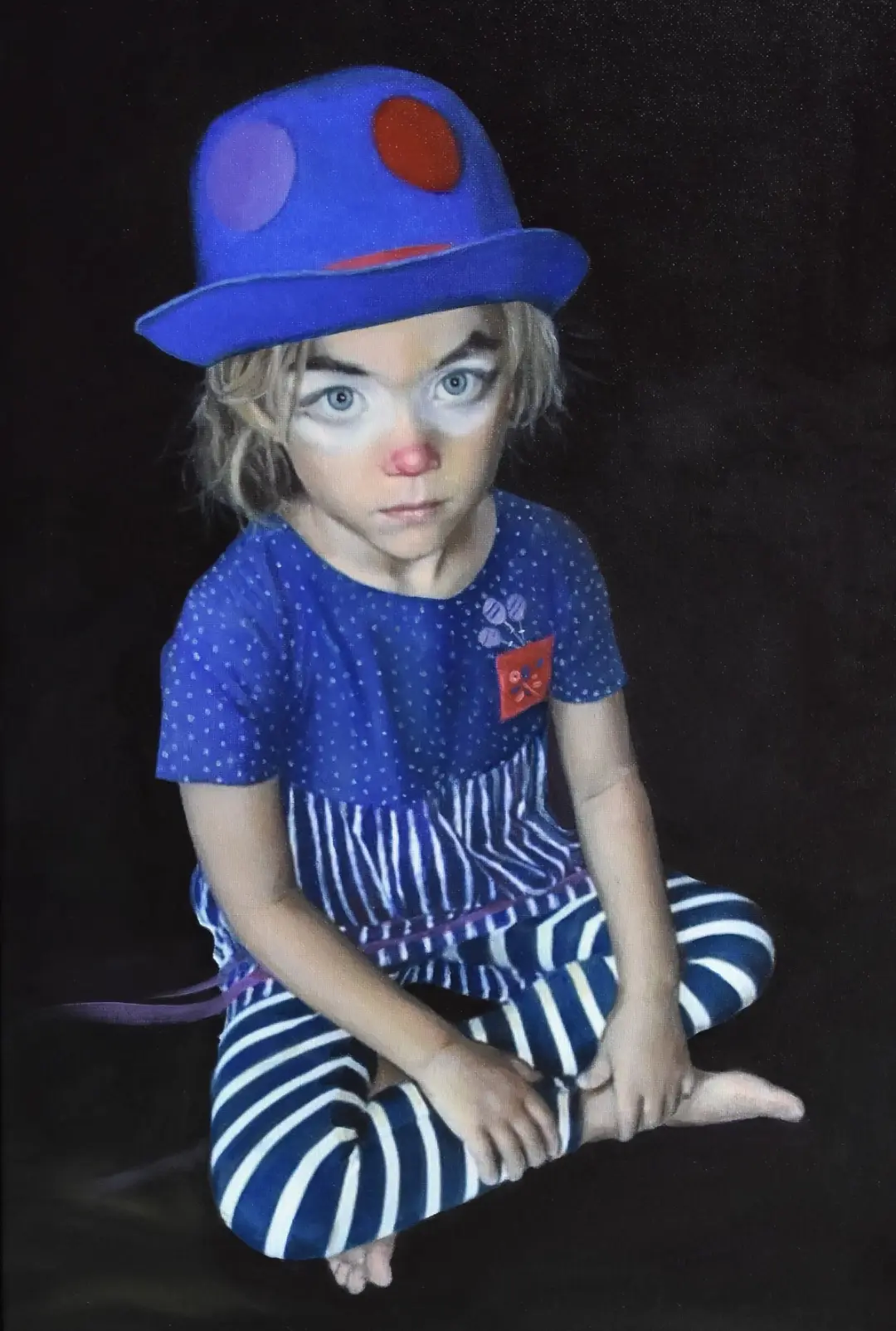 Enfant clown avec chapeau bleu et maquillage, regard direct sur fond noir.