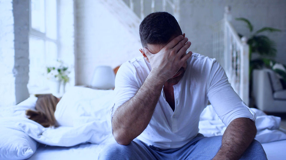 Homme assis au bord d’un lit, la tête dans la main, évoquant les troubles de l’érection, les troubles de l’éjaculation et la pression de performance.