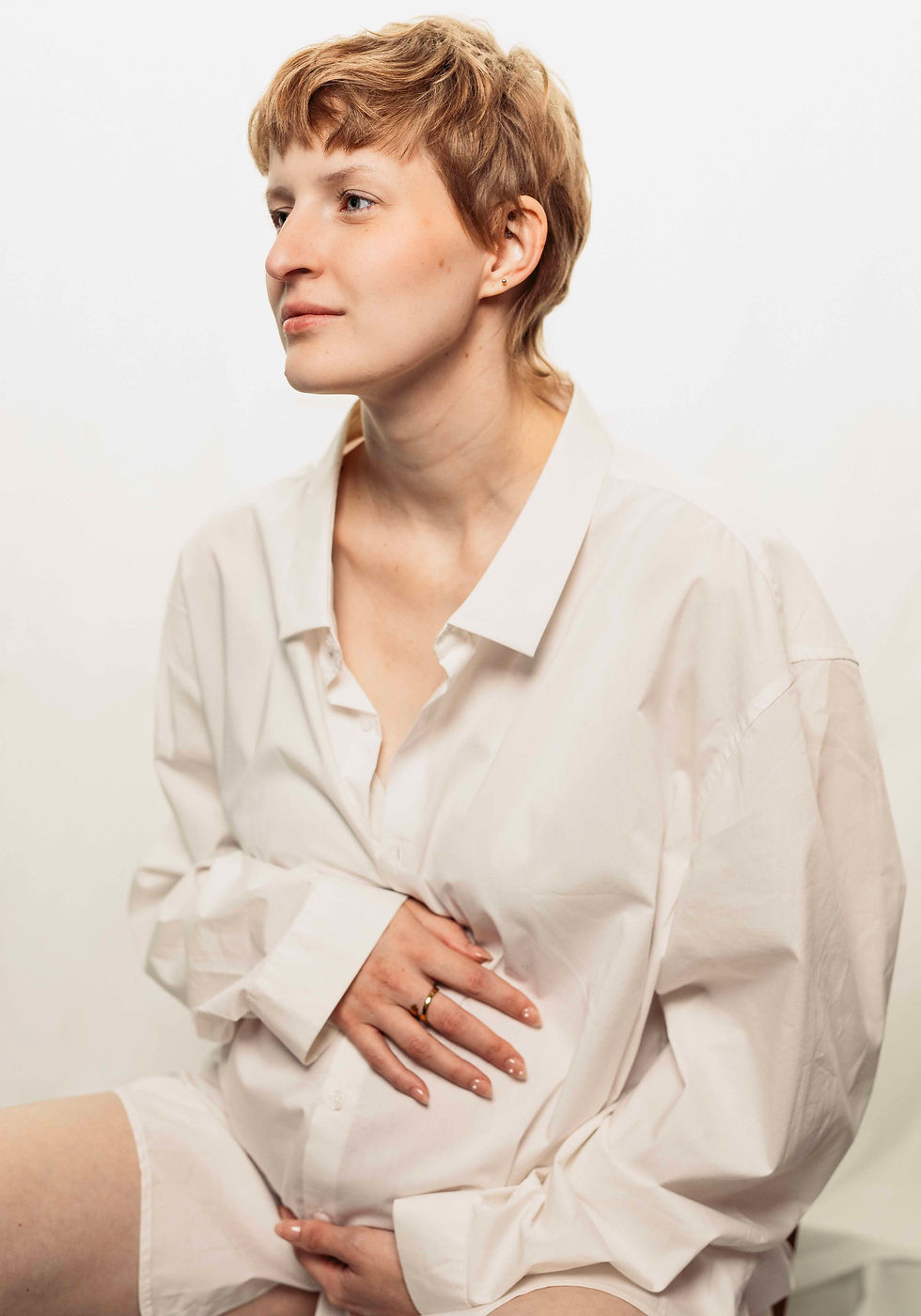 A person with short hair sits wearing a white shirt, hands resting on their stomach. The background is plain white, evoking a calm mood.