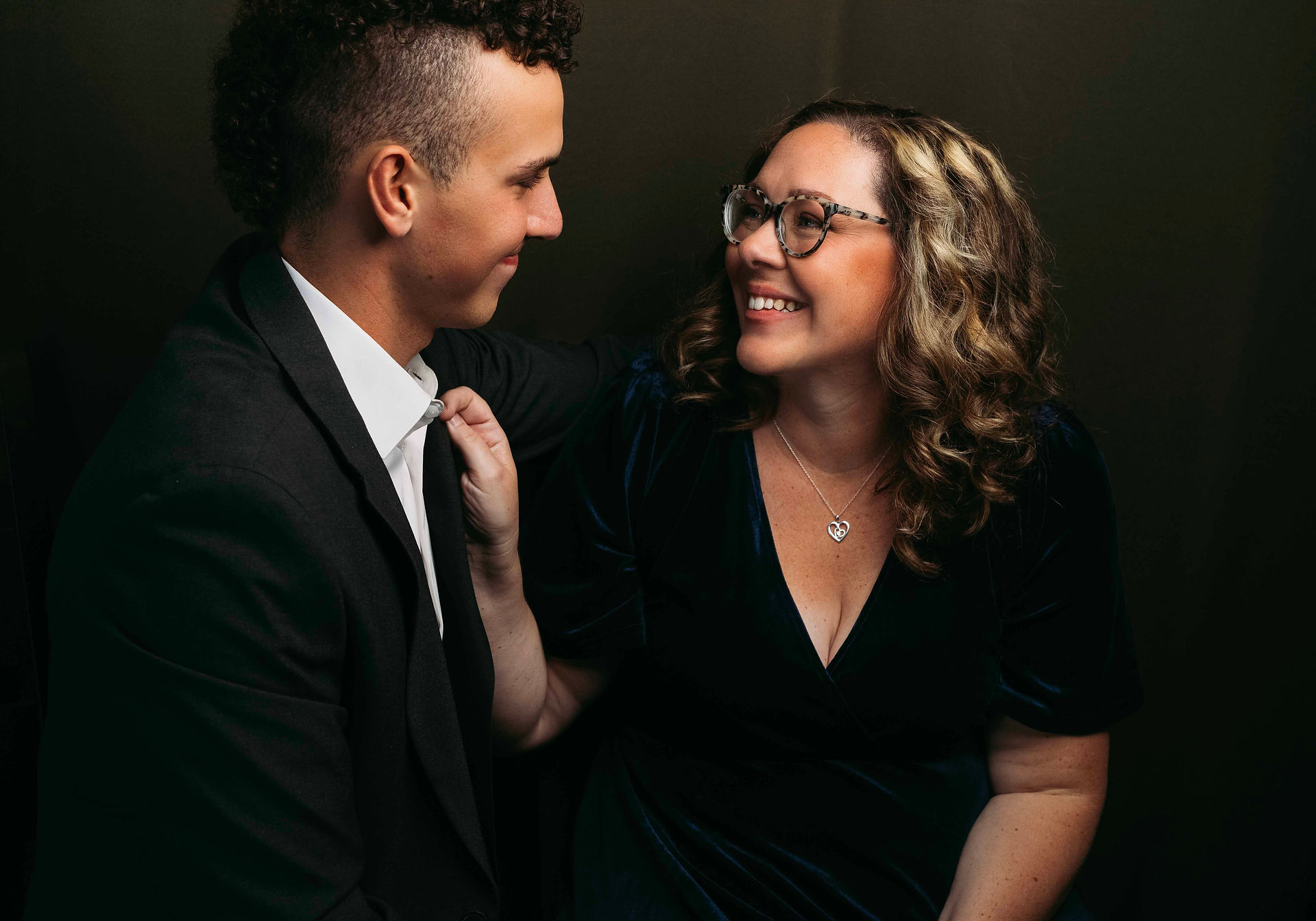 Alyssa straightening the suit of her son as they smile together during family photoshoot.