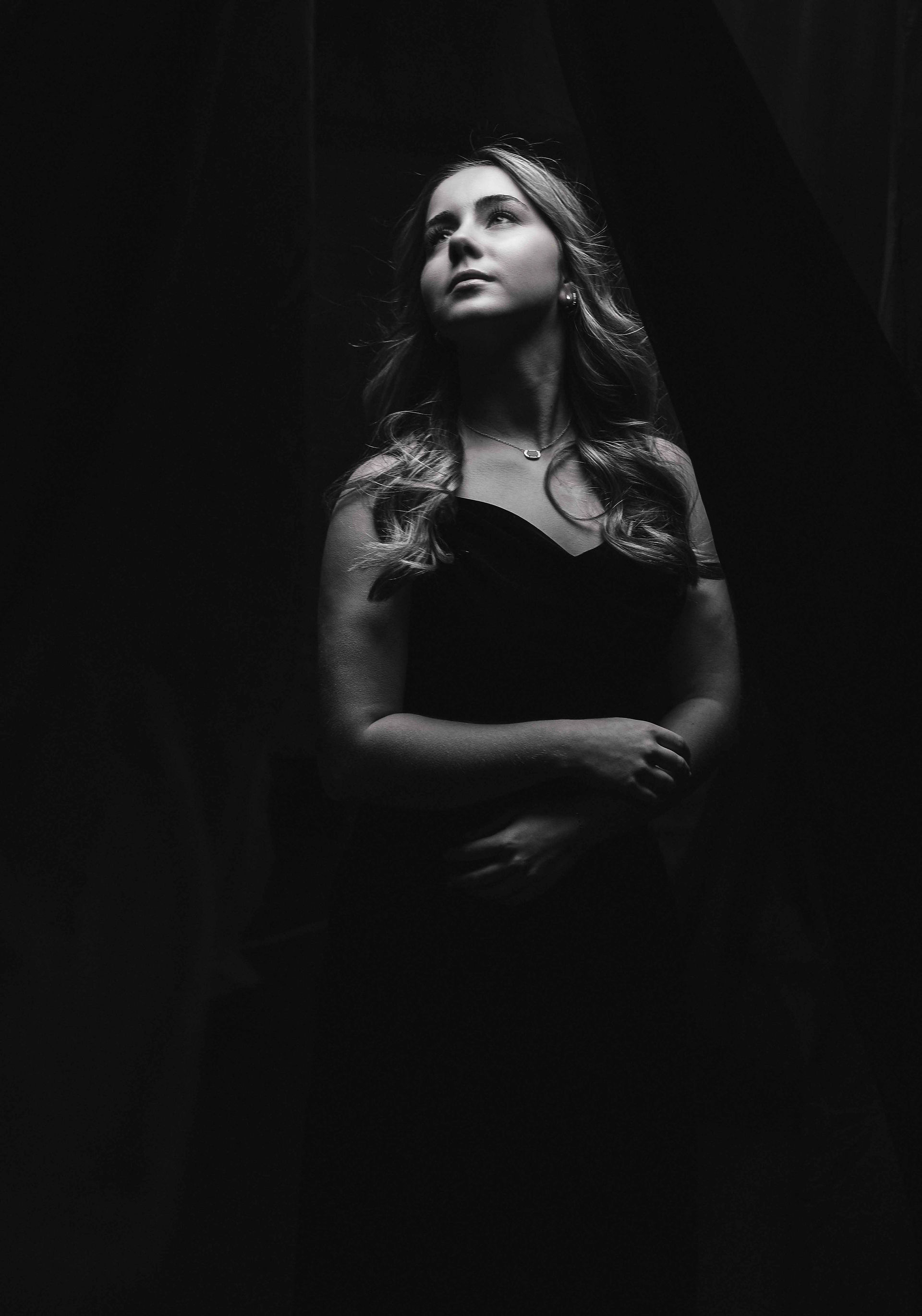 Black and white picture of senior girl in black dress on black background.