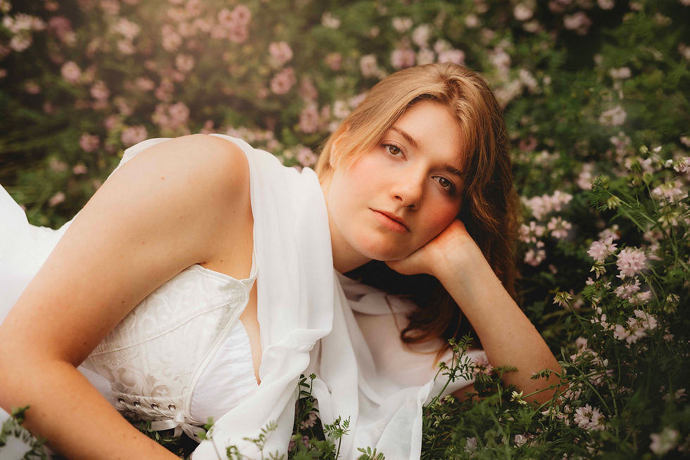Young woman in a white dress in pink wildflowers, resting her head on her hand, with a calm, dreamy expression.
