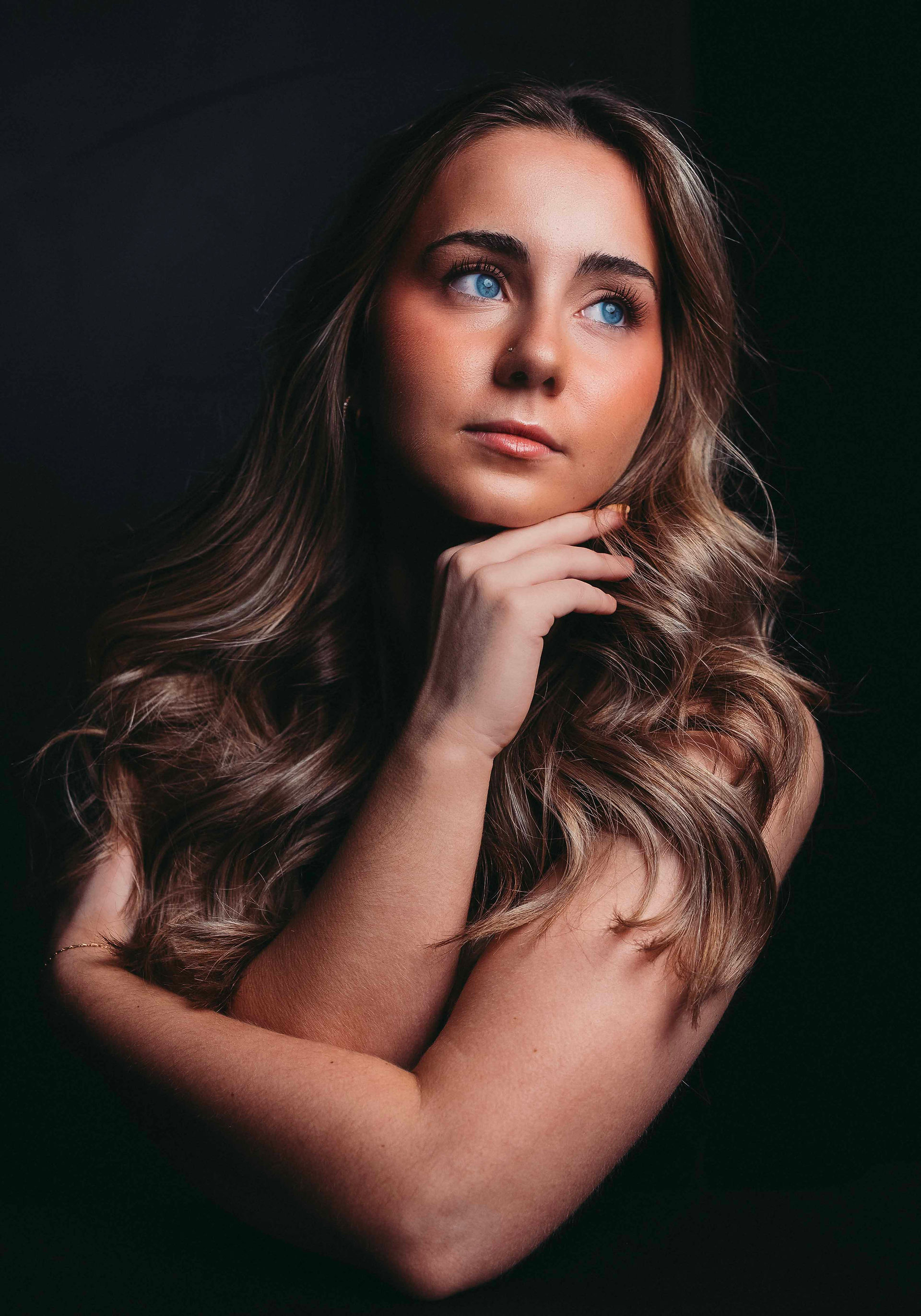 Crystal blue eyed young woman with her arms wrapped around herself looking off to the side as she contemplates life.