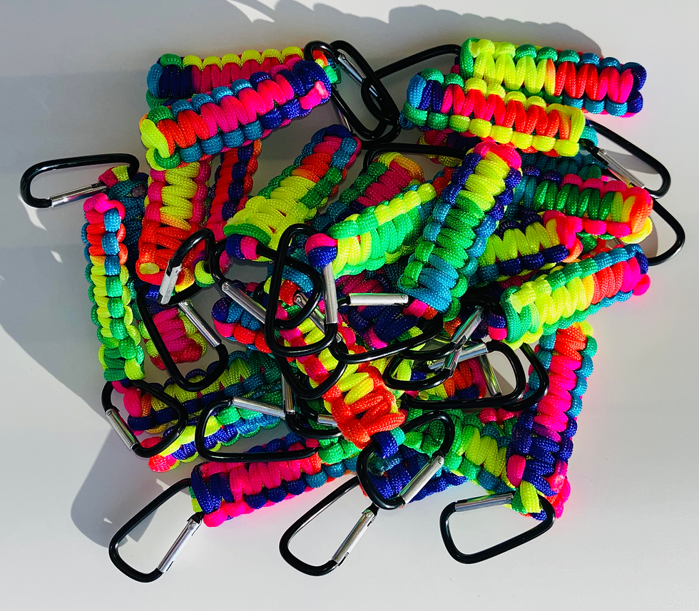 Een grote stapel felgekleurde TugTools van regenboog-paracord met zwarte karabijnhaken op een lichte achtergrond.