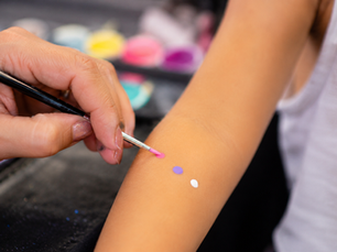 Maquilleuse professionnelle réalisant un test cutané sur le bras d’un enfant avant un maquillage artistique pour peaux sensibles.