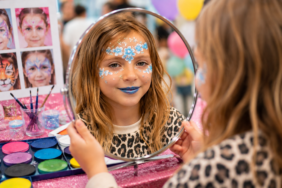 Petite fille souriante découvrant son maquillage floral bleu et blanc dans un miroir lors d'une animation maquillage enfant. Son visage est décoré de fleurs délicates, de paillettes scintillantes et de détails élégants, dans une ambiance festive et colorée.