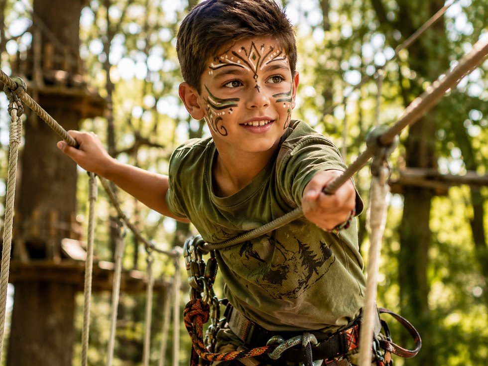 Enfant maquillé en aventurier explorateur évoluant sur un parcours accrobranche en forêt. Son maquillage artistique mêle arabesques, points décoratifs et motifs tribaux dans des tons verts, blancs et noirs. Équipé d'un harnais de sécurité, il traverse un pont de cordes entre les arbres sous une lumière naturelle chaleureuse, dans une ambiance d'aventure et de découverte.