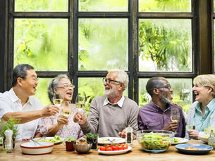 Groupe de seniors souriants réunis autour d’un repas convivial, échangeant et partageant un moment de bonne humeur. Cette scène illustre le lien social, l’amitié, les rencontres et l’esprit de communauté que souhaite développer Nous les Seniors.