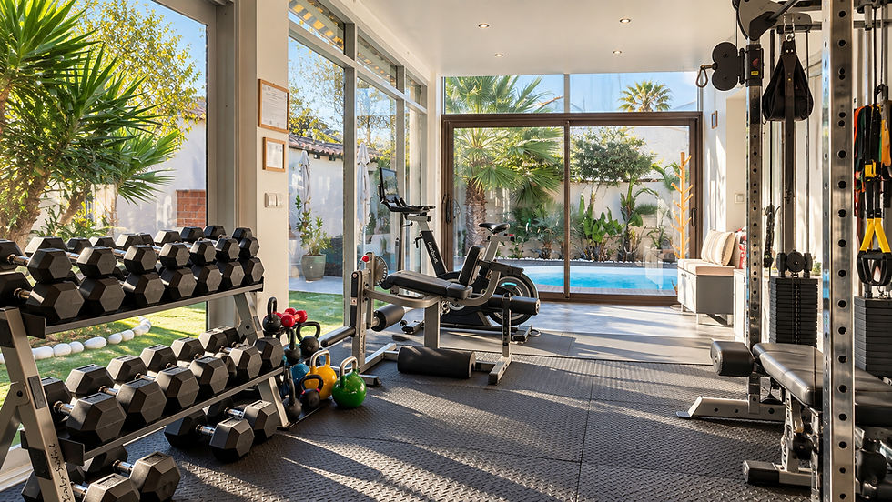 Salle de sport et de bien-être lumineuse à Pérols dans l’Hérault, équipée de matériel de musculation et donnant sur un jardin avec piscine.