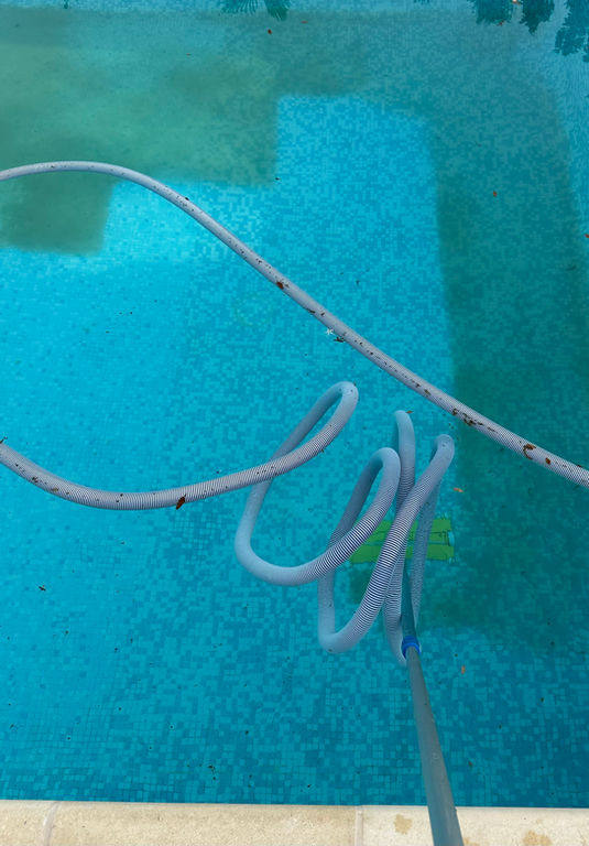 Entretien complet de piscine : nettoyage du fond et de la surface par un technicien avec balai aspirateur pour une eau cristalline.