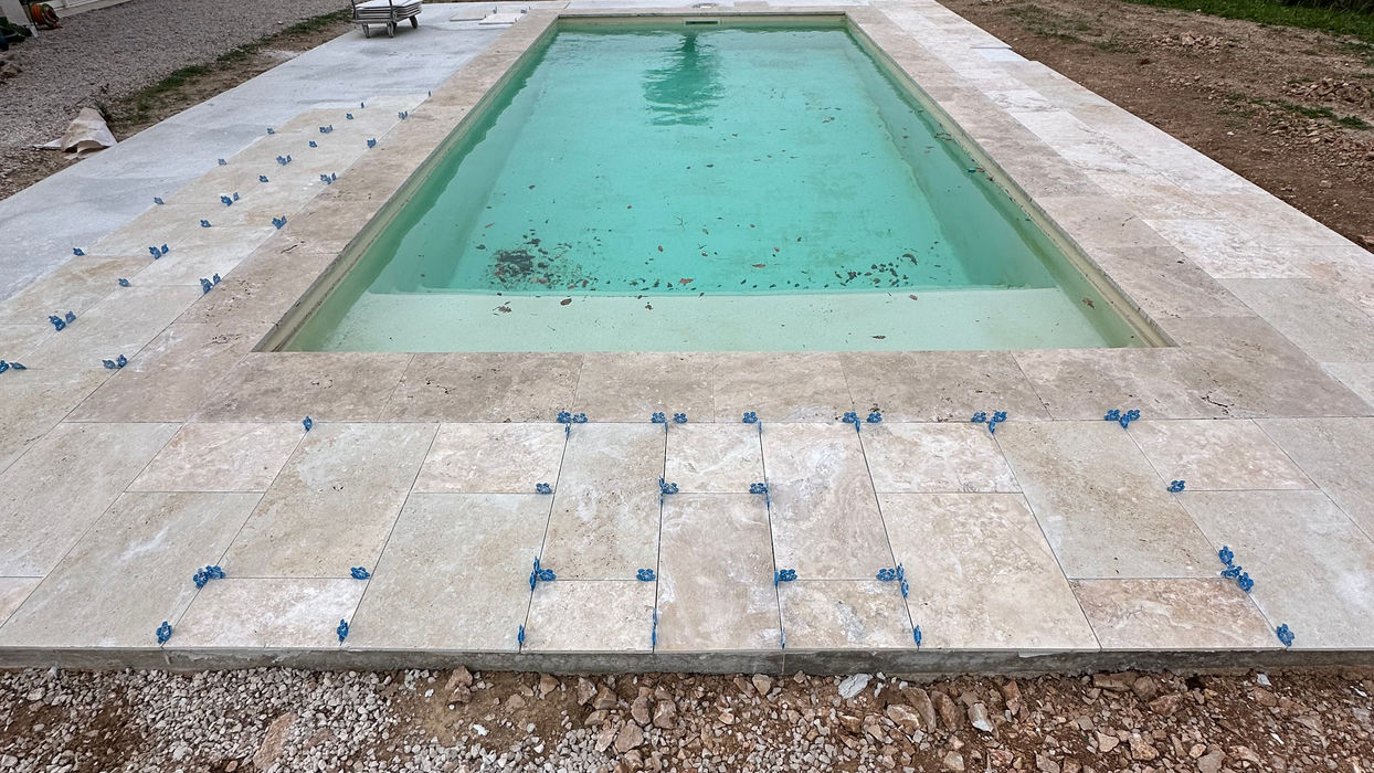 Pose de travertin autour d’une piscine avec croisillons de nivelage sur dalle béton lors d’une rénovation