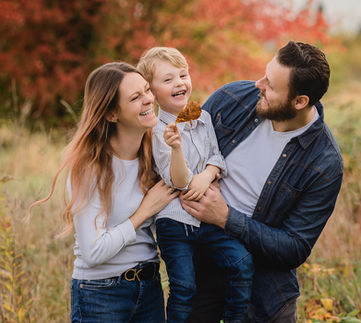 "Eine glückliche Familie posiert für ein Fotoshooting in einer herbstlichen Naturkulisse. Die Bäume sind in warmen Herbstfarben getaucht, während die Sonne durch die Blätter scheint."