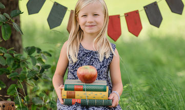 Mädchen sitzt auf einer Bank mit Büchern in der Hand, passend zur Einschulung.