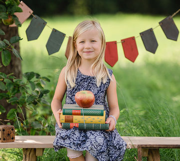 Mädchen sitzt auf einer Bank mit Büchern in der Hand, passend zur Einschulung.
