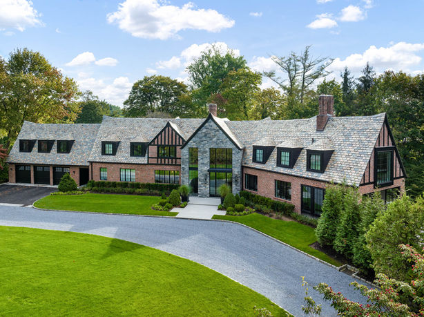 Aerial view of a Tudor-style residence with a brick and stone façade, landscaped lawn and curved driveway