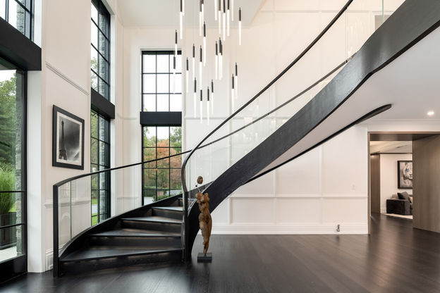 Sculptural curved staircase with a black balustrade and white panelled wall in a Scarsdale residence.