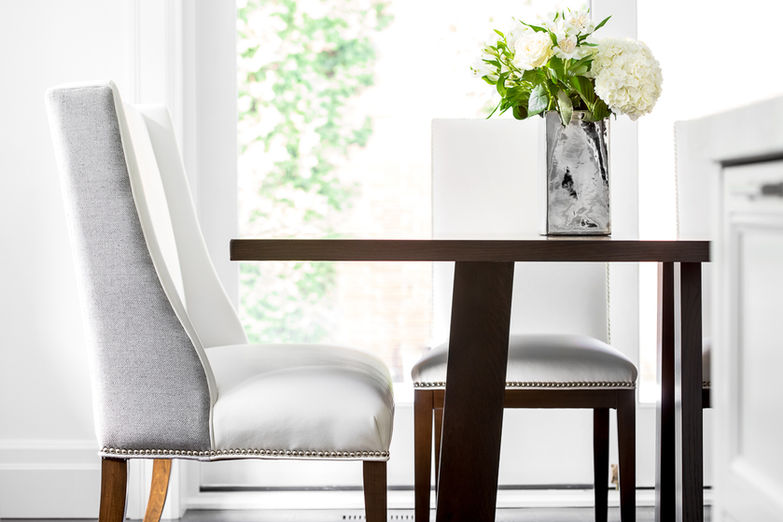 Dining table detail with upholstered chairs, dark wood accents and a white floral arrangement.