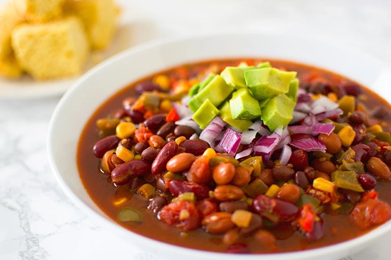 Slow Cooker 3 Bean Chili in a white bowl on a marble surface with corn bread in the background