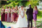 Meg Senior | FAQs for wedding celebrants | Couple at the front of their wedding ceremony, with their celebrant who wears a bright pink and purple dress covered in love hearts
