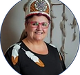 Chief Knockwood smiles while wearing her tall headdress and a black shirt with white feathers on the shoulder