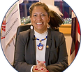 Chief Beaudin sits at a desk with her hair pulled back, her hands clasped in front of her white shirt under a sand colored blazer. She wears beaded neclace and earings.