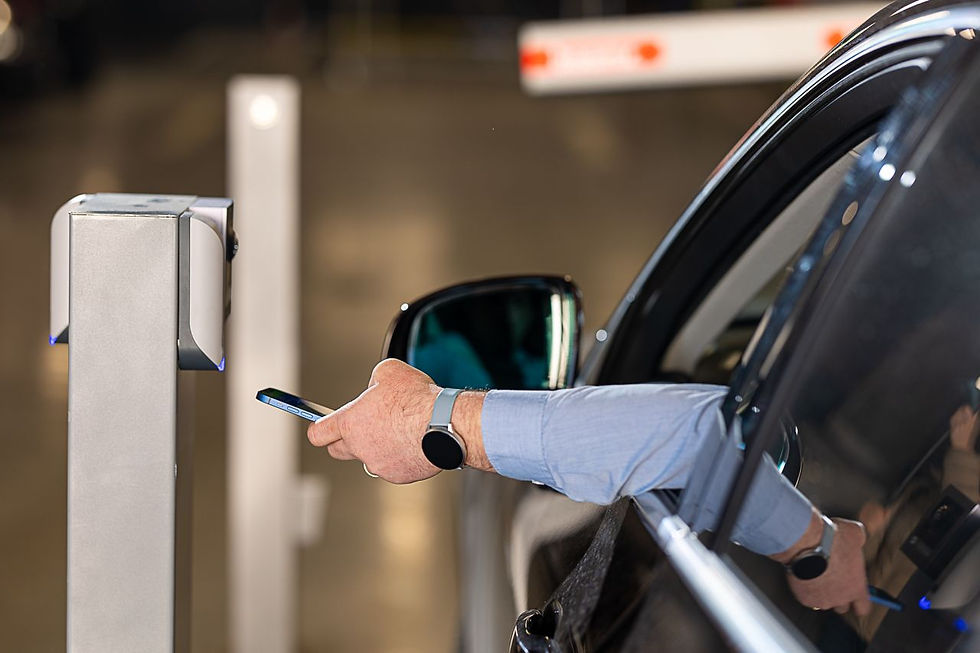 Conducteur présentant son smartphone à un lecteur de contrôle d’accès pour ouvrir une barrière de parking depuis son véhicule.