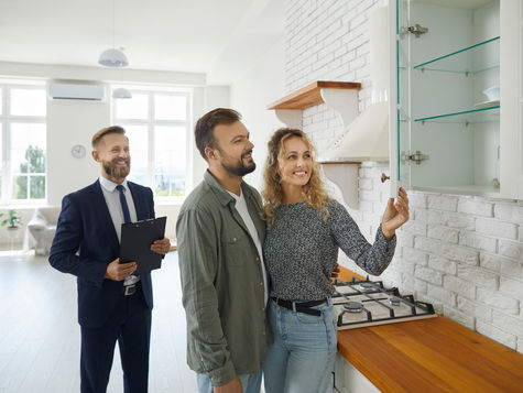 A couple explores the modern kitchen of their potential new home, guided by a smiling real estate agent.