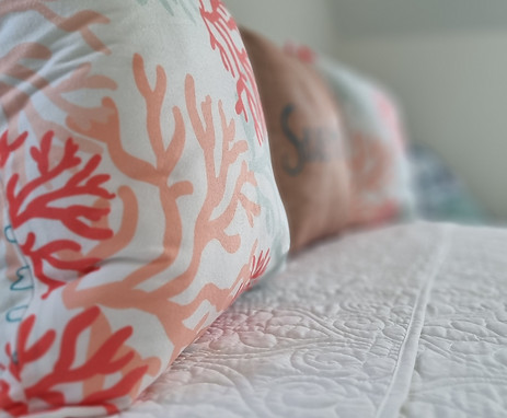 Close-up of a decorative pillow on a bed at Bon Suites Cayman, featuring a white background with a red-orange coral pattern.