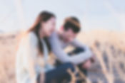 A smiling couple sitting outdoors in a sunny field, enjoying a lighthearted moment together.