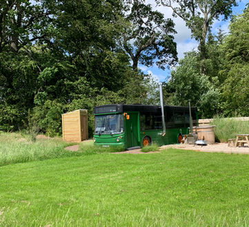 Eco Bus 1 wide landscape view, green bus on lawn with trees and wooden shed