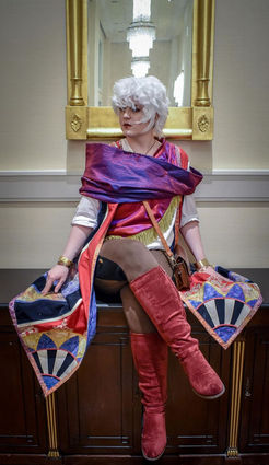 Emer sitting on a surface wearing a cosplay outfit indoors