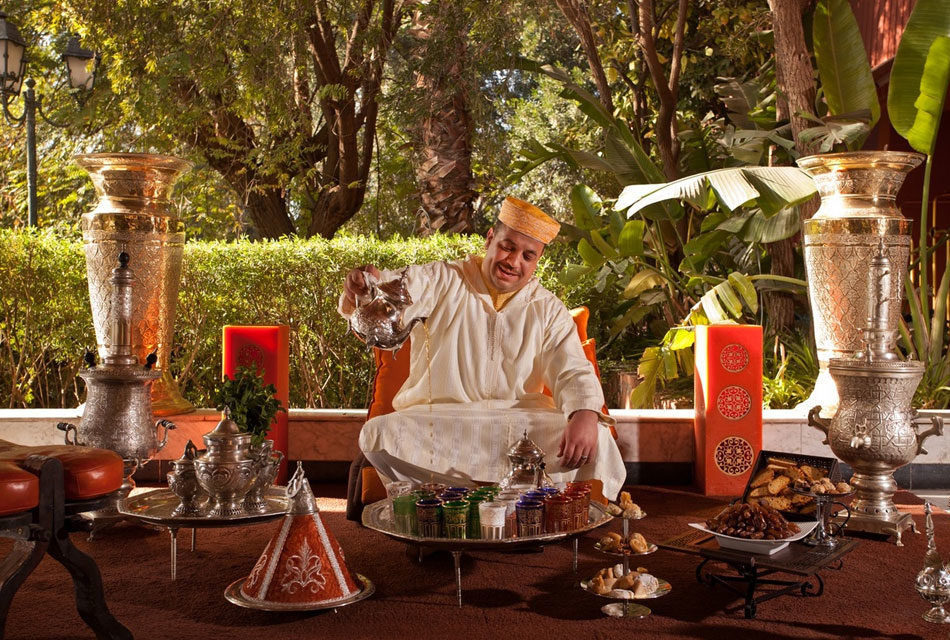 A man in a traditional Moroccan outfit sitting on a chair with a large vase.