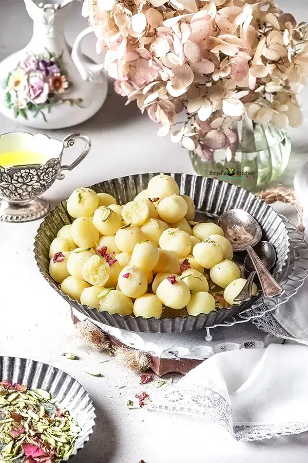 A bowl filled with soft, spongy white balls of rasgulla, an Indian dessert made with cottage cheese dumplings simmered in a sugar syrup. The bright pink syrup encases the delicate rasgullas, creating a visually appealing and mouthwatering treat.