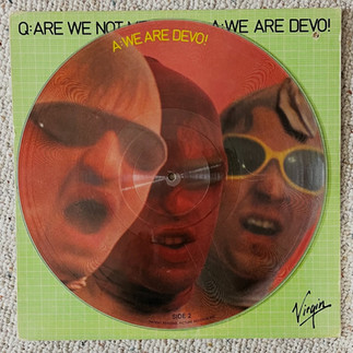 Green Devo vinyl sleeve with three men in glasses screaming; text reads Q:ARE WE NOT MEN? A:WE ARE DEVO! Virgin logo.