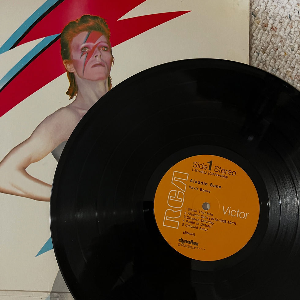 A black vinyl record with an orange RCA Victor 'Side 1' label for David Bowie's Aladdin Sane, resting in front of the album's iconic cover showing Bowie with the red-and-blue lightning bolt across his face.