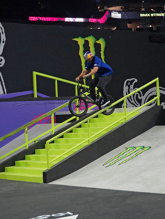 A BMX rider in a blue jersey and Red Bull helmet grinds down the lime-green handrail of a stair set at X Games New Orleans 2026 during BMX Street.